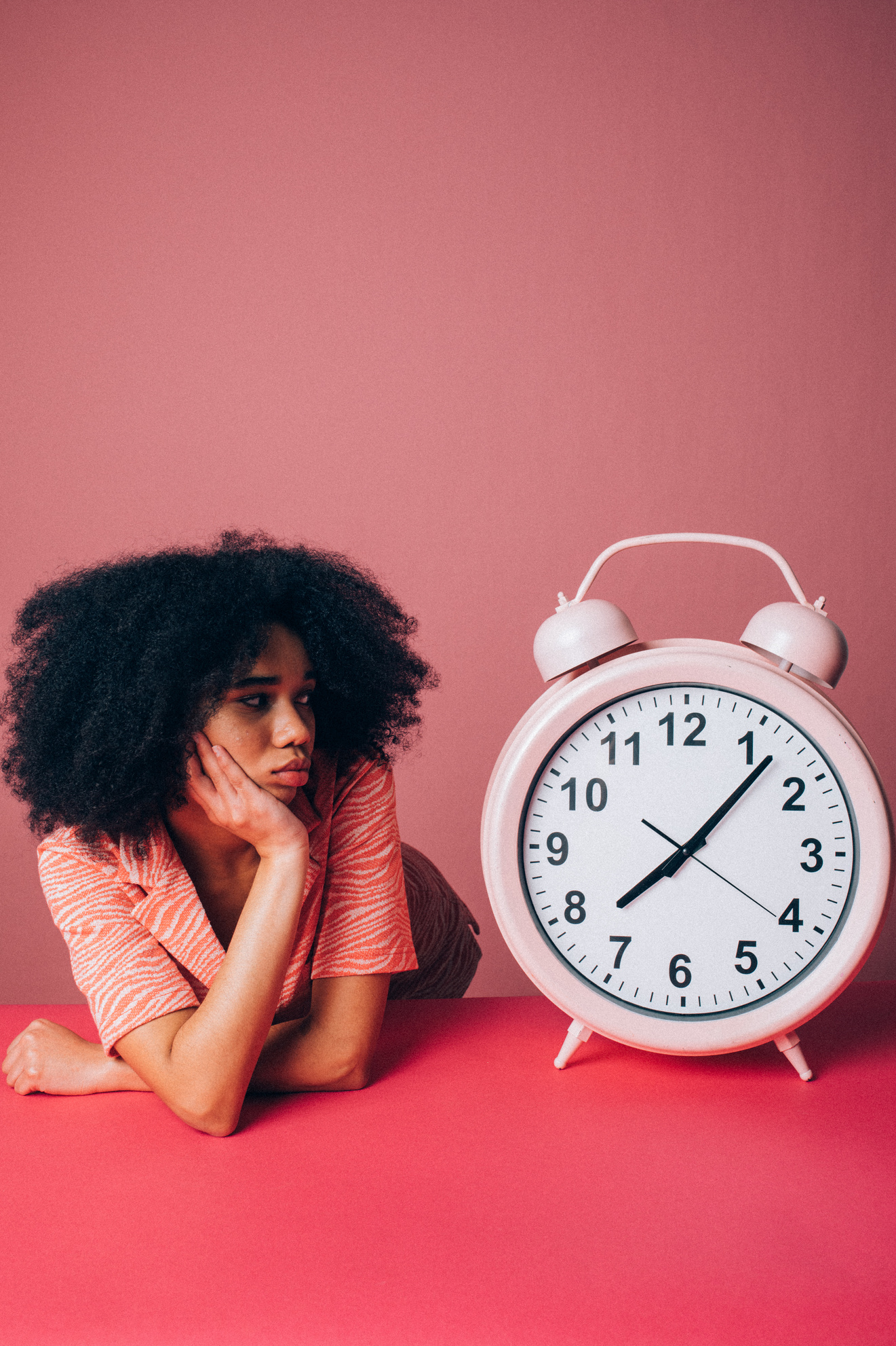 Woman in Pink Shirt Sitting Beside White Alarm Clock